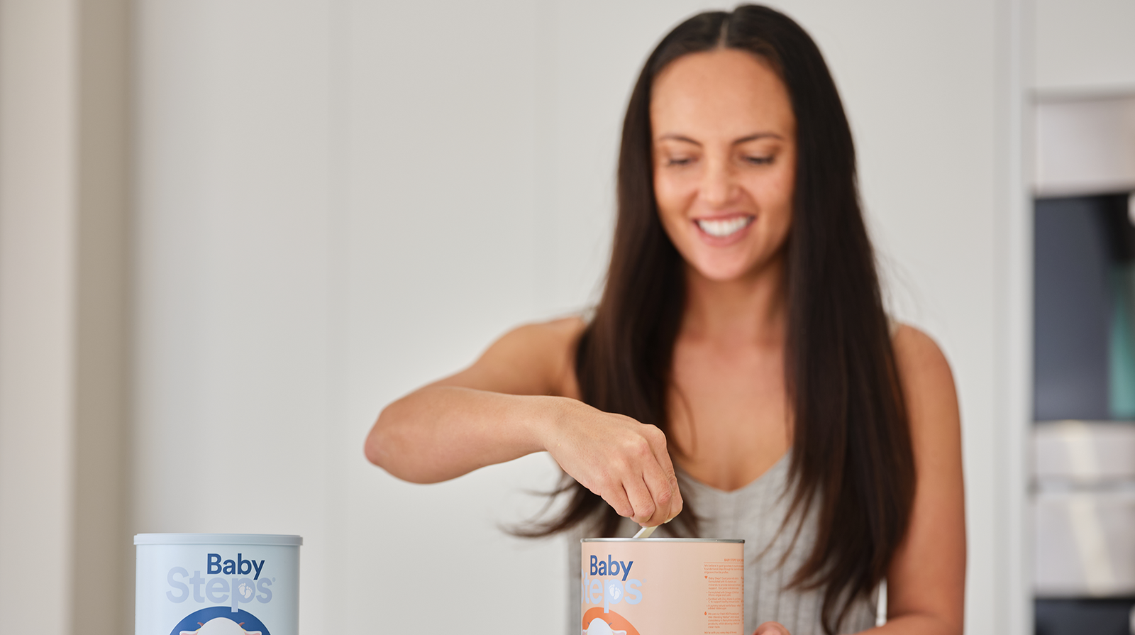 Mother opening Baby Steps Stage 4 can. Baby Steps Stage 3 can sitting next to it.