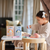 Female toddler playing with wooden toys on a table. Baby Steps Stage 3 & 4 cans sitting on table.